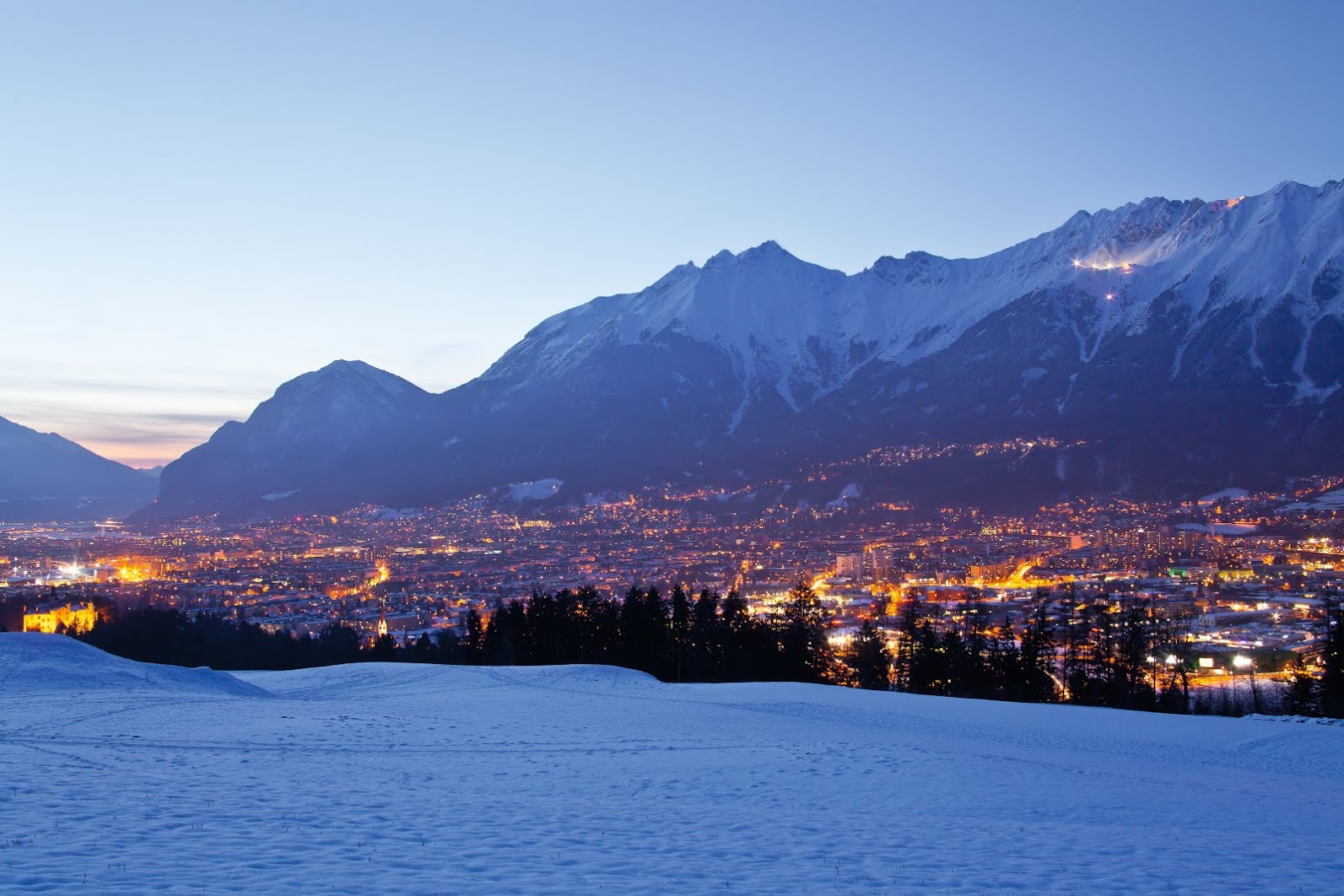 Innsbruck al anochecer, con la ciudad iluminada y las montañas nevadas detrás