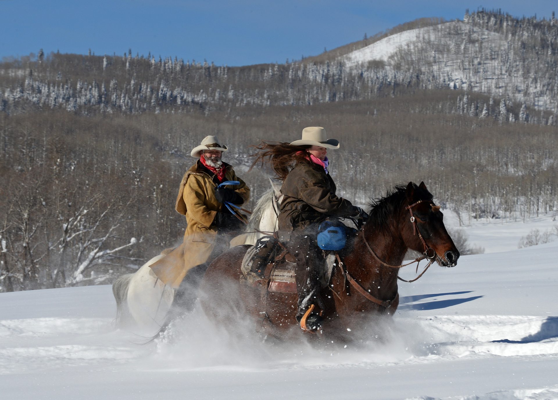 Dos jinetes con sombrero vaquero cabalgando sobre la nieve