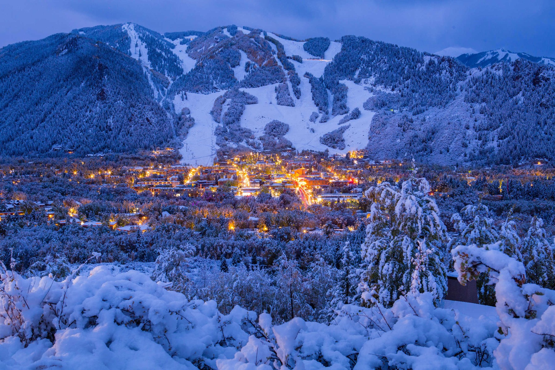 El pueblo de Aspen iluminado al anochecer, nevado, con las pistas de esquí detrás