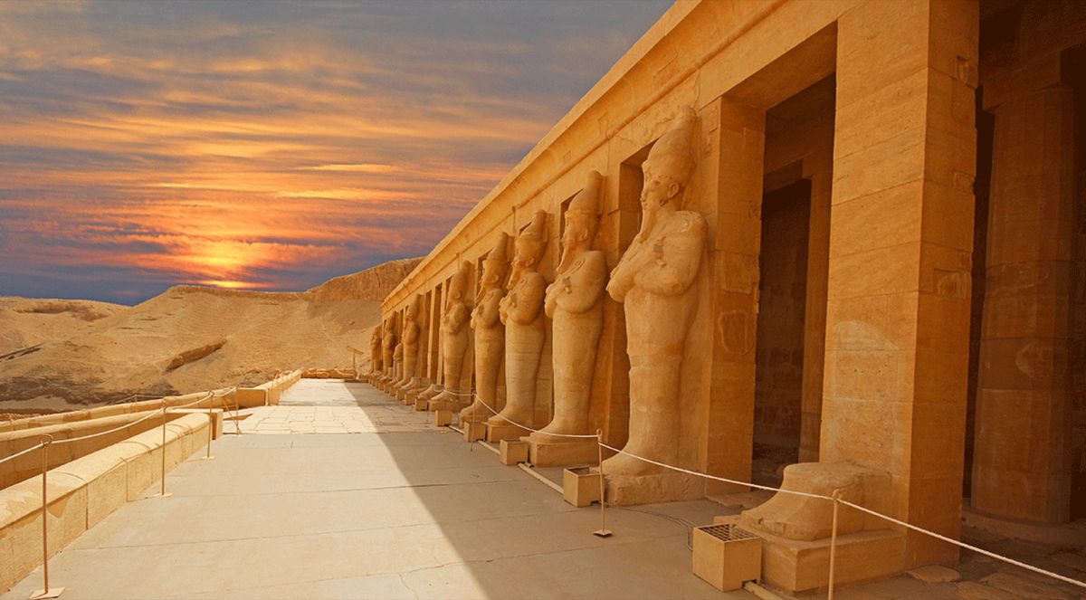 Estatuas colosales en la fachada de un templo egipcio, con el sol bajo sobre el desierto
